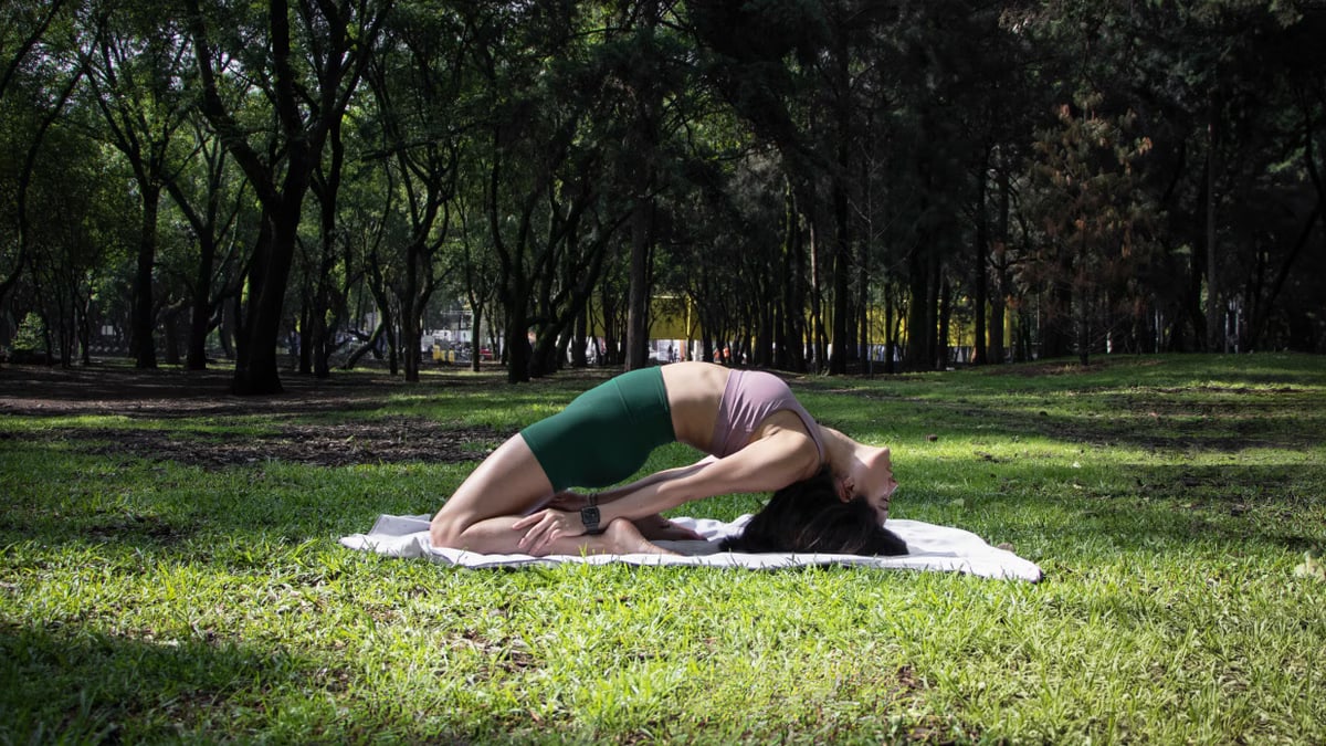 Woman performing a yoga pose on a sunny day in a lush green park in Ciudad de México.